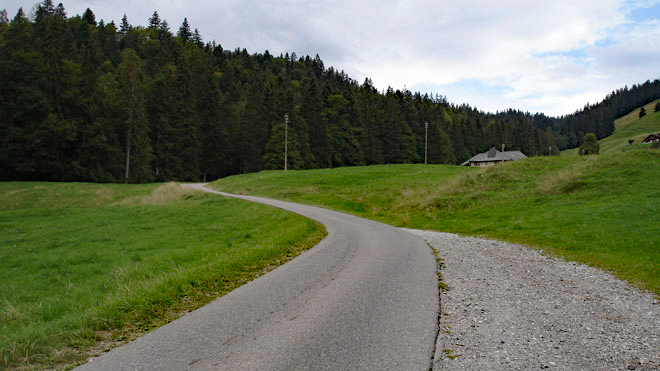 In weit geschwungenen Kurven steigt die Strasse an vereinzelzen Alphütten vorbei